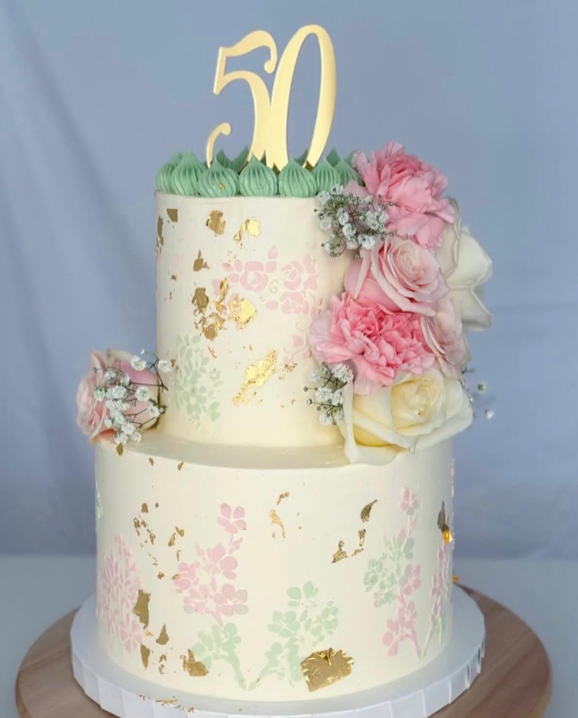 Tvåvåningstårta för 50-årsdag med guldskylt och fräscha blommor